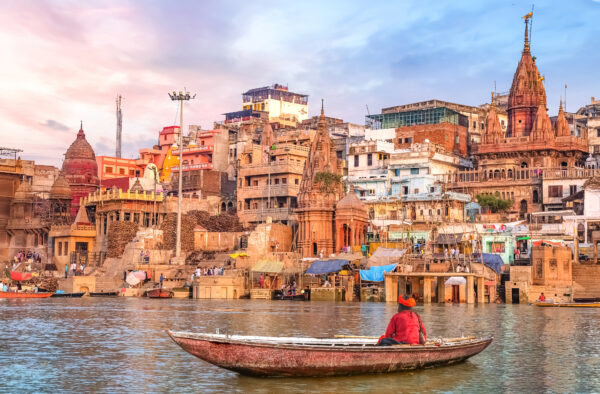 Hindu sadhu sitting on a boat overlooking Varanasi city architecture at sunset